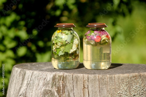 Two glass jars with sun tea. Solar tea is water heated by solar energy, which contains various tree leaves, flowers, medicinal herbs, fruits. 