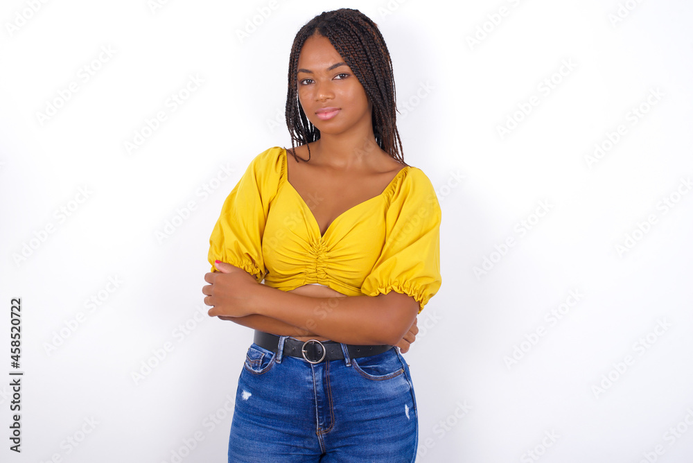 Confident afro american woman with braids wearing sexy yellow t-shirt on white wall with arms crossed looking to the camera Confident afro american woman with braids wearing sexy yellow t-shirt on white wall with arms crossed looking to the camera