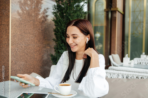 The girl sits in a cafe using technology. the girl looks at a teleon in a cafe at a table. photo