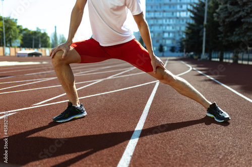 Young Caucasian sportive man, male athlete, runner practicing alone at public stadium, sport court or running track outdoors. Summer sport games.
