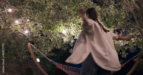 Carefree woman having fun rotating under illuminated tree with arms outstretched at night