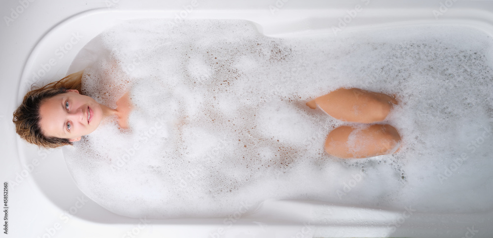 Young woman lying in warm bath with foam top view Young woman lying in warm bath with foam top view