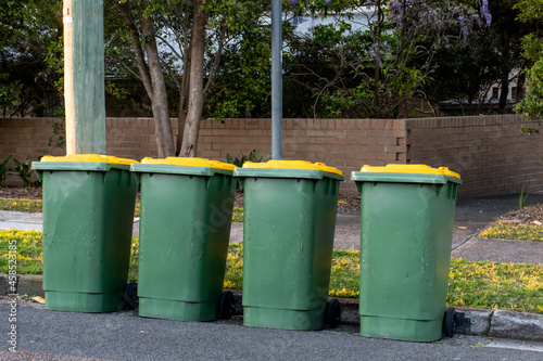 Australian garbage wheelie bins with colourful lids for recycling household waste on the street kerbside for council rubbish collection. © Daria Nipot