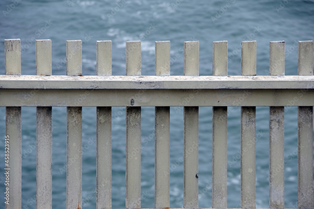 Close-up view of a section of weathered white wooden picket fence with the ocean visible behind