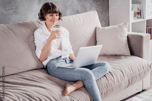 Photo portrait woman wearing white shirt using computer typing message drinking coffee at home on couch