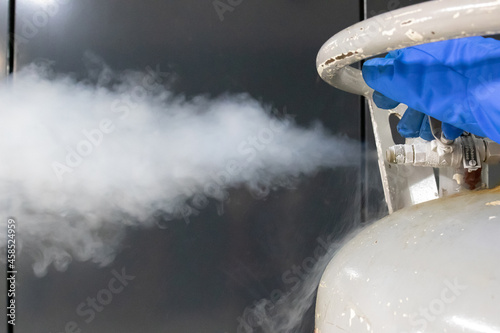 Operator hand in blue protective glove releasing the pressure valve on a liquid nitrogen tank. Close up shot. photo