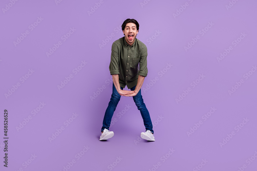 Full size photo of funny funky happy young man hold hands together good mood enjoy isolated on purple color background Full size photo of funny funky happy young man hold hands together good mood enjoy isolated on purple color background