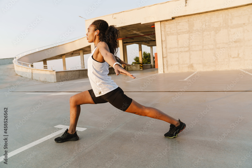 Fototapeta premium Black sportswoman listening music while working out at parking outdoors