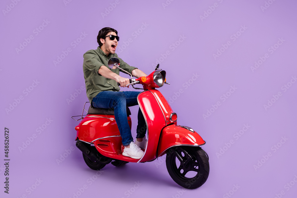 Full length photo of crazy happy cheerful young man wear sunglass ride bike isolated on violet color background Full length photo of crazy happy cheerful young man wear sunglass ride bike isolated on violet color background