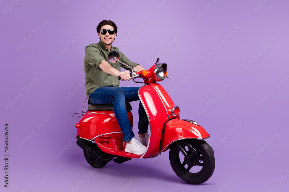 Full body photo of positive happy cheerful man wear sunglass ride motorbike isolated on violet color background Full body photo of positive happy cheerful man wear sunglass ride motorbike isolated on violet color background