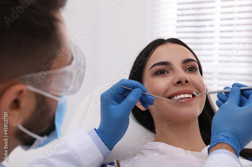 Dentist examining young woman s teeth in modern clinic