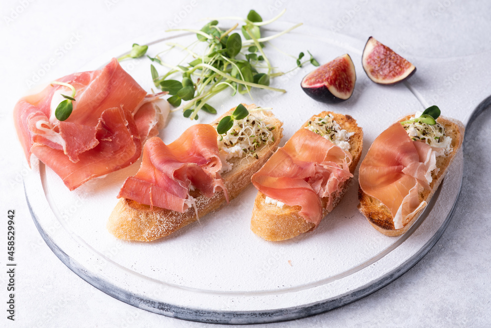 Crostini with prosciutto on a white background, antipasto of ham, ricotta and microgreens.
