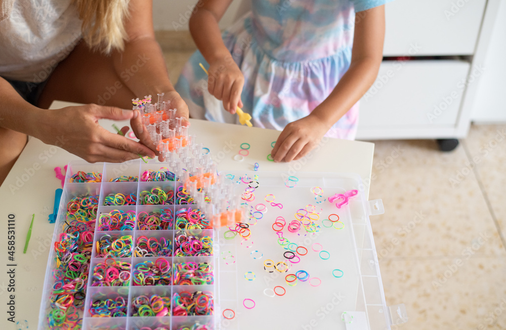 Hands of mother with daughter playing and making accessories bracelet from silicone rubber bands. collect necklace by hook. hobby woman and girl. make gift together Hands of mother with daughter playing and making accessories bracelet from silicone rubber bands. collect necklace by hook. hobby woman and girl. make gift together
