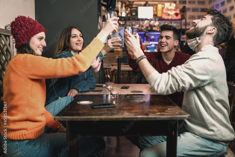 Young people toasting beer wearing lowered face mask