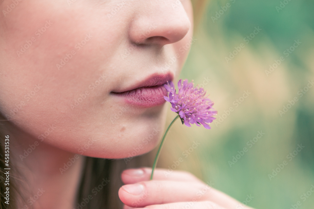 portrait of beautiful young woman among yellow field with red flower at her lips