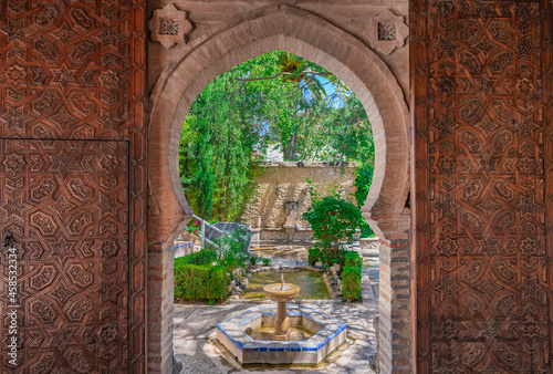 Puerta árabe abierta hacia un hermoso jardín con fuentes, estanques y vegetación.
