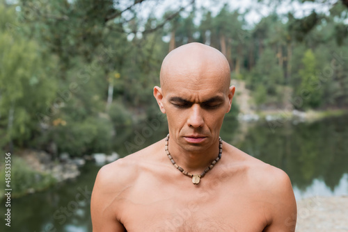 shirtless buddhist in beads meditating with closed eyes in forest