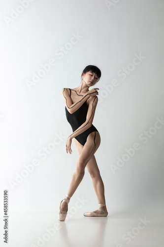 Young and graceful ballet dancer, ballerina dancing isolated on light gray studio background. Art, motion, action, flexibility, inspiration concept.