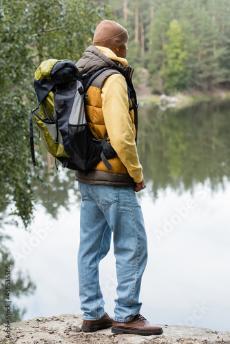 hiker in warm west and jeans looking at lake in autumn forest
