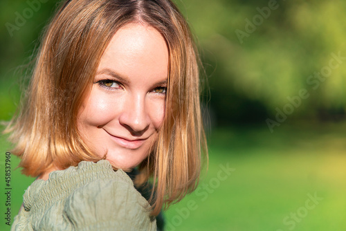Close up portrait of beautiful natural girl, young happy positive ginger attractive pretty woman is smiling outdoors at summer sunny day, looking at camera. Copy space.