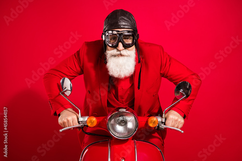 Photo of cool careful driver santa claus ride bike serious face wear goggles leather helmet suit on red color background photo