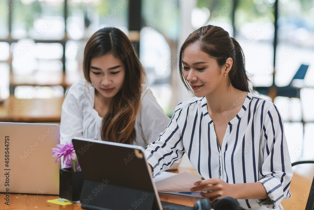 Team work of happy young Asian businesswoman analyze brainstorming together using a tablet the graph is placed on the office desk. Team work of happy young Asian businesswoman analyze brainstorming together using a tablet the graph is placed on the office desk.