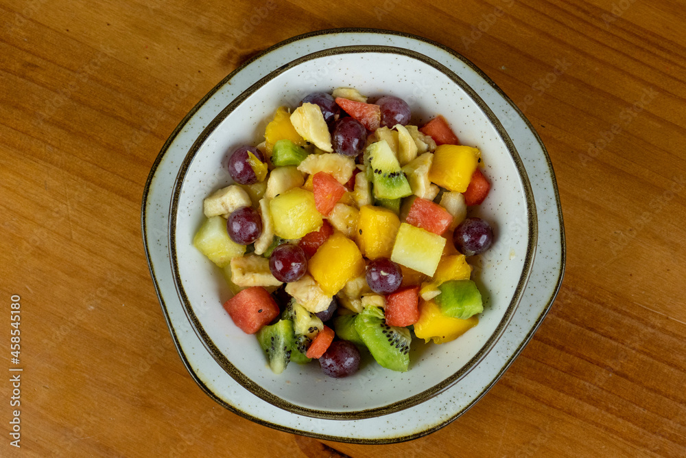 refreshing fruit salad , natural colors served in crockery container and small white plate , white wooden background in photo taken from above with space for text on the side