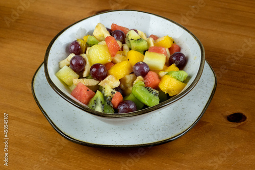 refreshing fruit salad with natural cereals served in crockery container and small white plate , wooden background in photo made in side angle with space for text on the side