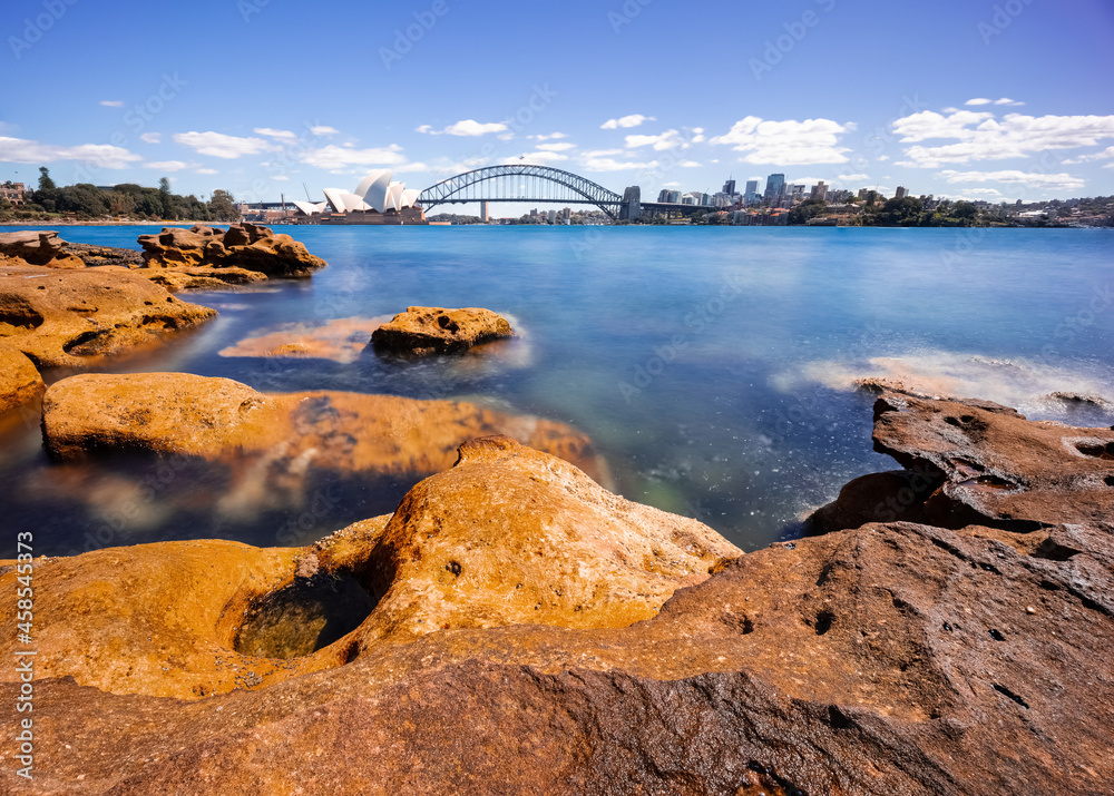 Sydney Harbour with nice rocks in the foreground the soft waves crashing on the shore and the beautiful harbour foreshore as a backdrop NSW Australia