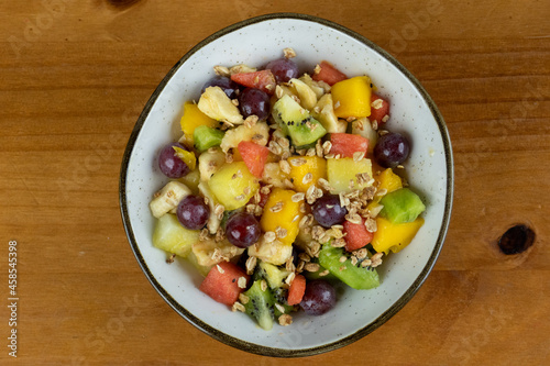 fruit salad with natural cereals served on white tableware , wooden background in photo taken from above with space for text on the side