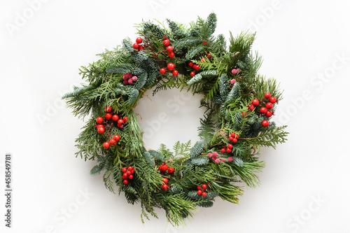 Festive Christmas wreath of fresh natural spruce branches with red holly berries isolated on white background. New Year. Top view. Traditional decoration for Xmas holiday.