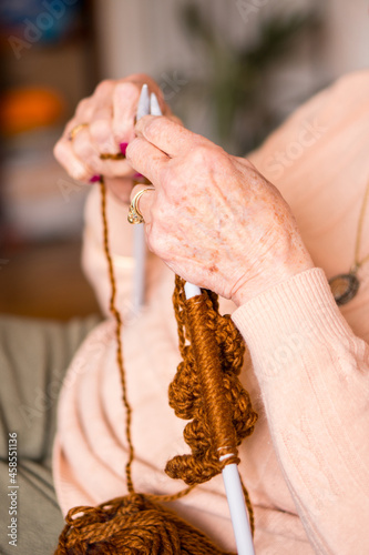 Vertical image of an old woman knitting with brown wool. Female old hands. Grandma hobby