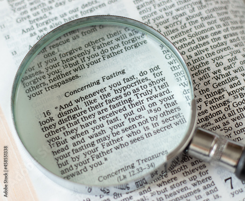 Open Holy Bible with a magnifying glass on passages about fasting.  Christian fast, repentance, and humility before God and Jesus Christ. Biblical concept. A closeup.