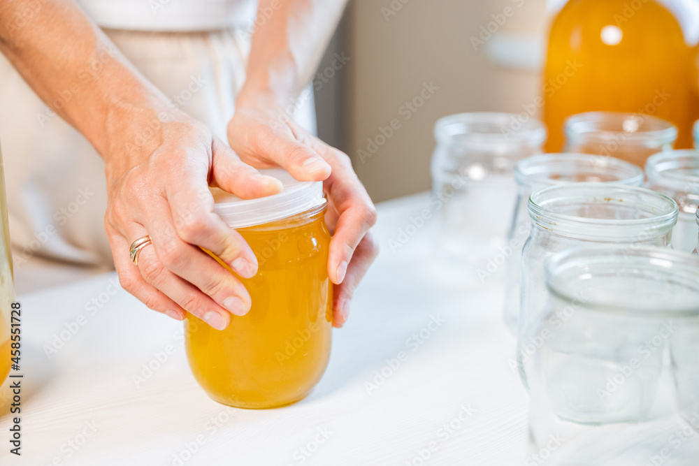 Woman's hands close the lid of a jar of honey standing on a white table and next to a saucer with a spoon Woman's hands close the lid of a jar of honey standing on a white table and next to a saucer with a spoon