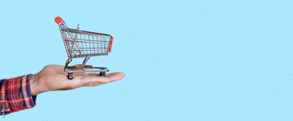 Supermarket trolley in hand on empty colored background. Online grocery shopping and selling concept