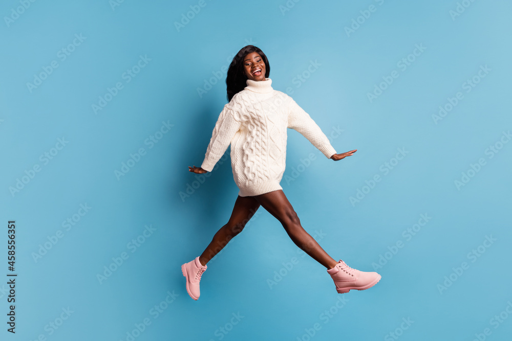Full length photo of shiny dark skin lady wear white winter outfit walking jumping isolated blue color background