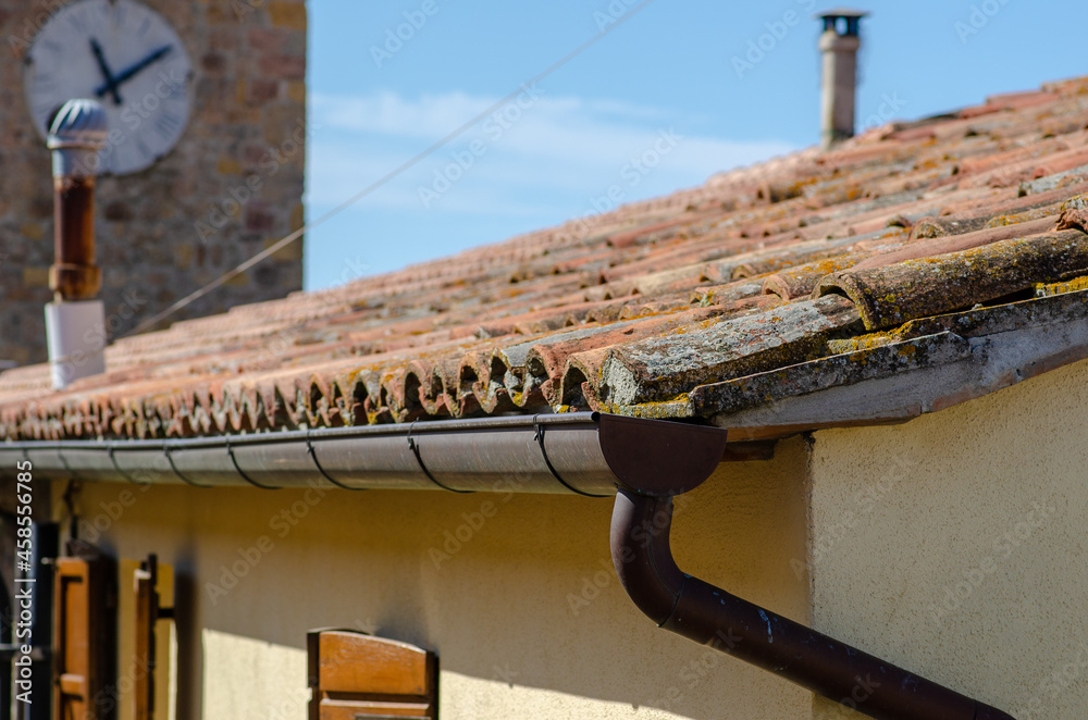 House building with pitched roof with clay tiles and tiles, visible rainwater drainage pipes