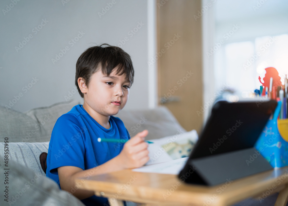 Schoolboy using colour pen drawing on white paper sheet, Young kid using tablet for school homework online on internet, Happy mixed race child enjoy painting. Home Education Schoolboy using colour pen drawing on white paper sheet, Young kid using tablet for school homework online on internet, Happy mixed race child enjoy painting. Home Education
