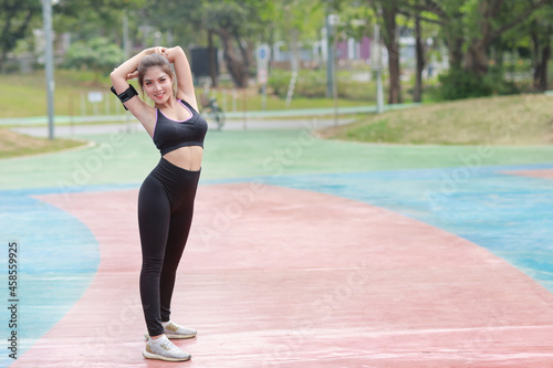 Athletic young healthy and beauty asian woman in sportswear standing and stretching outdoor for morning exercise. Active girl work out on biceps practice with mobile phone. Sport and lifestyle concept