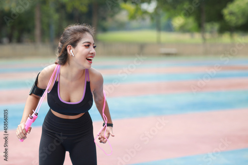 Athletic young asian woman in sportswear standing and skipping rope outdoor for morning exercise. Active and healthy girl workout on biceps exercise with tree background. Sport and lifestyle concept