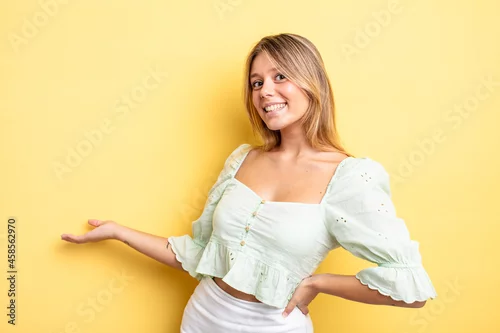 Obraz blonde pretty woman feeling happy and cheerful, smiling and welcoming you, inviting you in with a friendly gesture