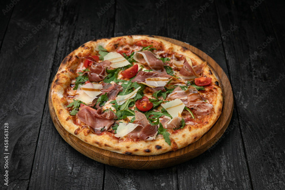 pizza with meat, parmesan and tomatoes on a wooden board on a dark table
