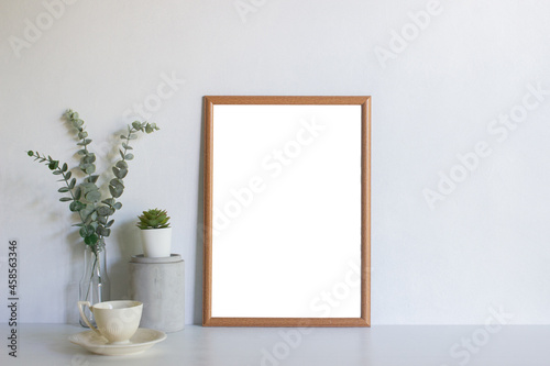 A blank picture frame with leaves on table.