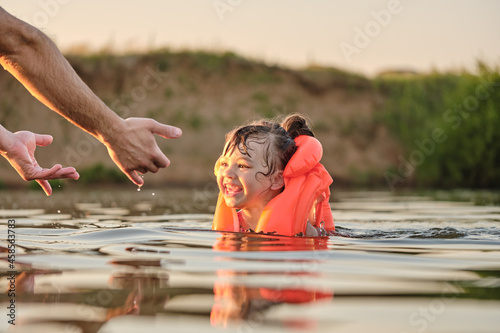 Father teaches daughter to swim. A child plays with his father during the summer vacation. A child in a life jacket. Water safety