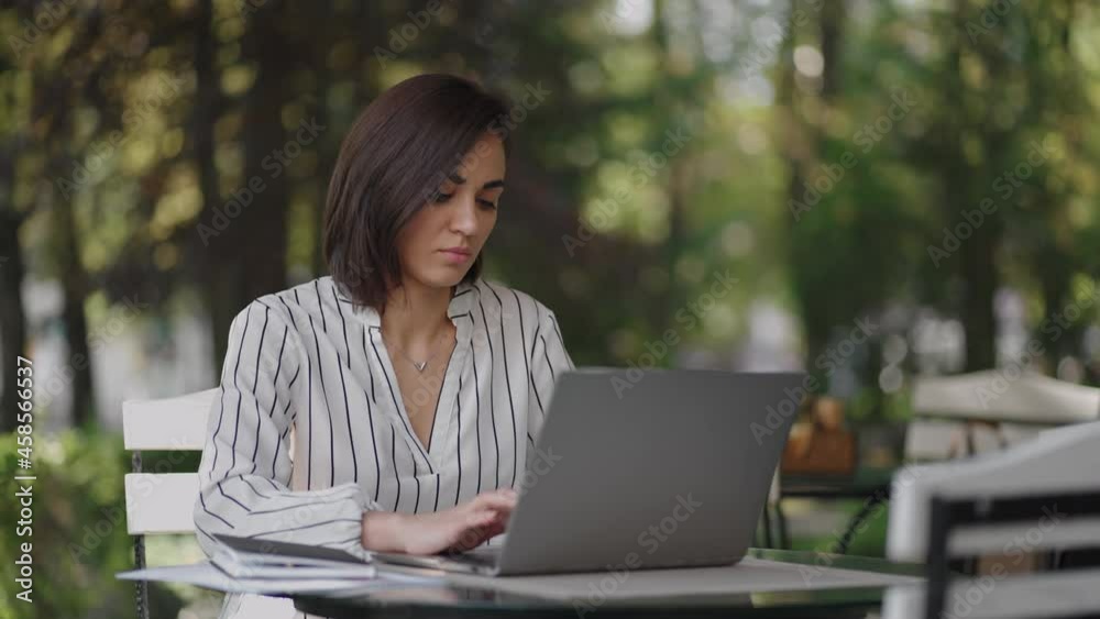 Portrait serious woman Brunette arabic Hispanic ethnic group sits at a table in a summer cafe with a laptop. types on the keyboard and undergoes online training, buys and deals with an Internet bank Portrait serious woman Brunette arabic Hispanic ethnic group sits at a table in a summer cafe with a laptop. types on the keyboard and undergoes online training, buys and deals with an Internet bank