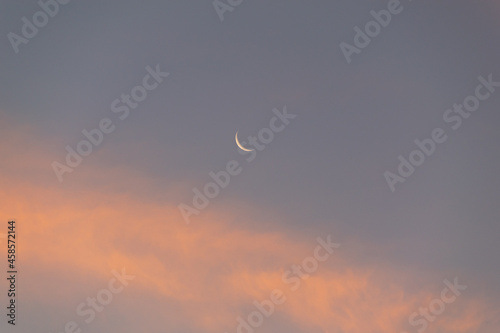Small new moon in a blue and orange sky 