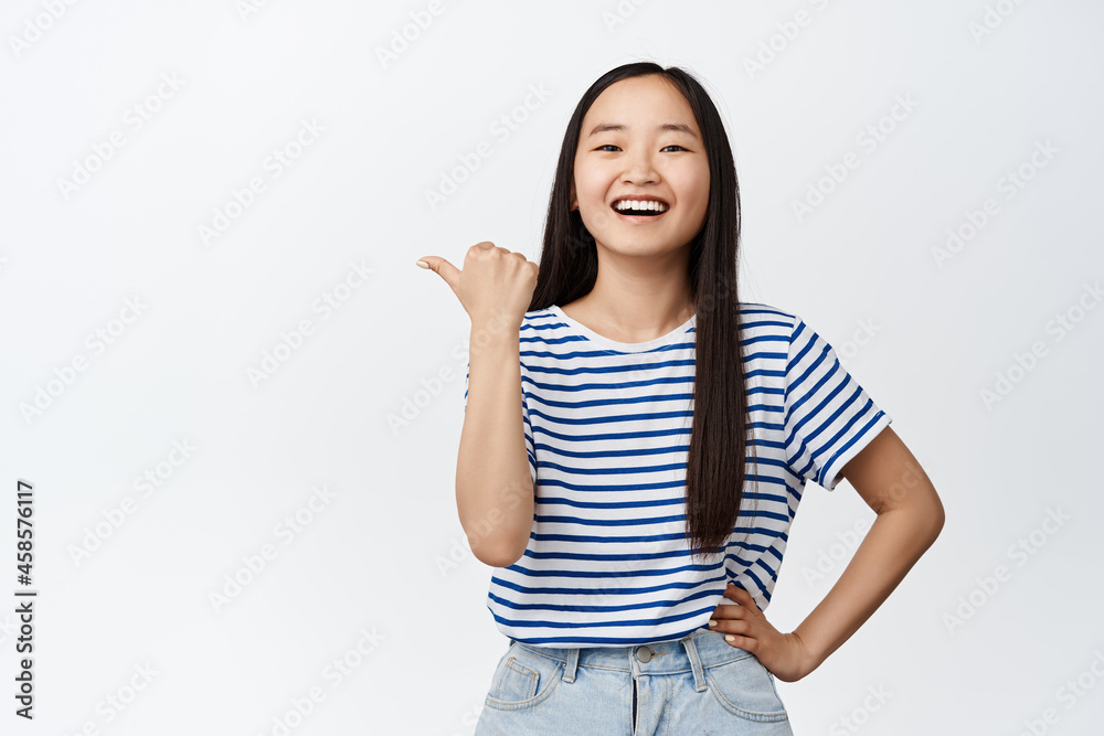 Portrait of beautiful korean girl pointing finger left and laughing, smiling and showing advertisement, recommending store, standing over white background Portrait of beautiful korean girl pointing finger left and laughing, smiling and showing advertisement, recommending store, standing over white background