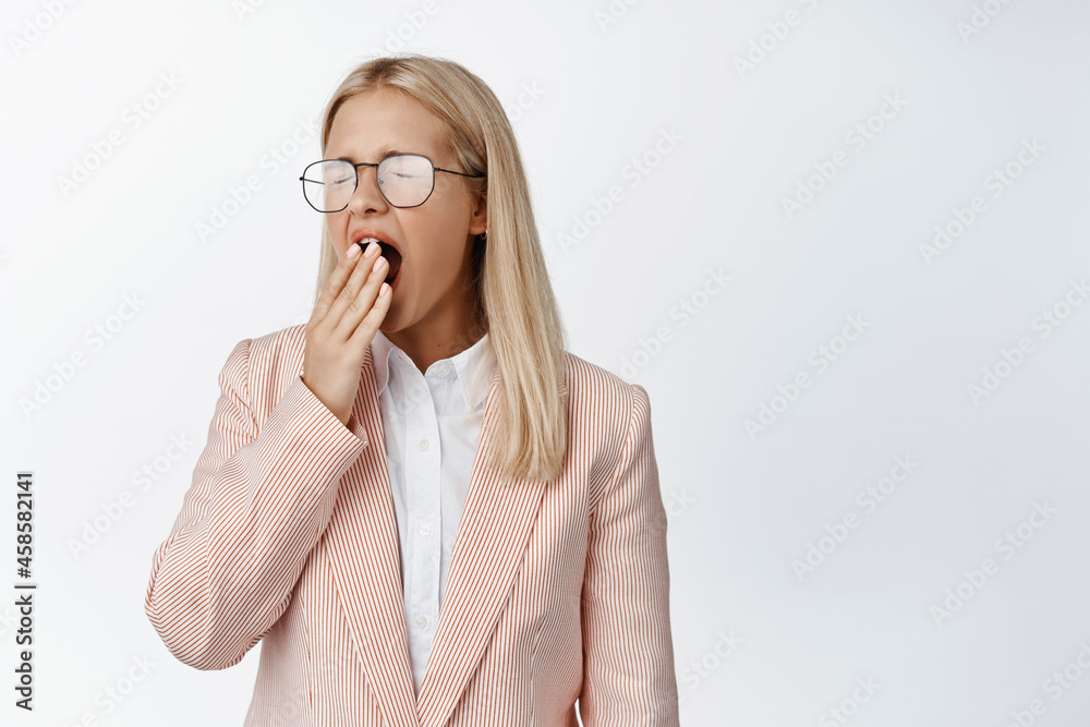 Tired female office worker yawning, cover mouth with hand, exhausted after work, standing in suit and glasses over white background