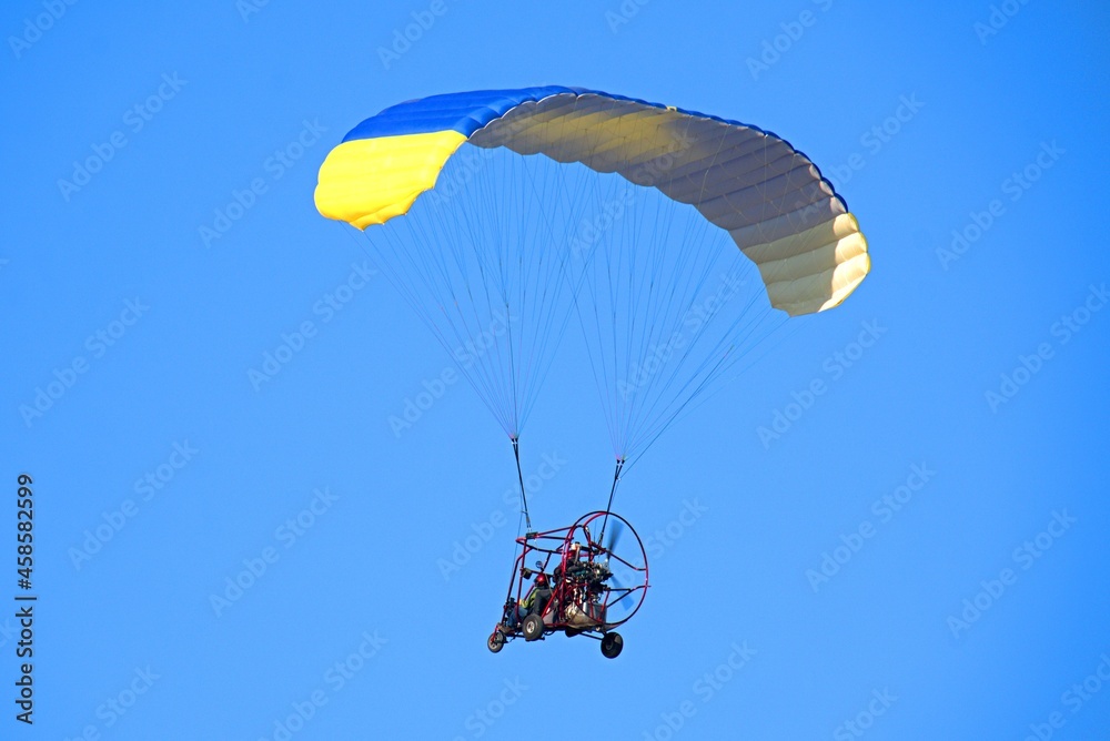 Yellow-blue paraglider in the blue sky Yellow-blue paraglider in the blue sky