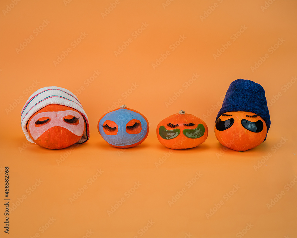 Four pumpkin with eye patches, facial mask and towel on orange background, copy space